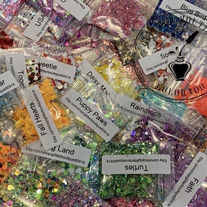 May include: A collection of small, clear plastic bags filled with various colors and shapes of glitter. Each bag has a label with a unique name, such as "USA", "Sweetie", and "Shooting Star". The image also includes a logo that says "Glitter Boutique Colorado".