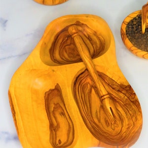 May include: A wooden serving dish with three compartments, one with a small wooden spoon. The dish is made of olive wood and has a natural, rustic finish.