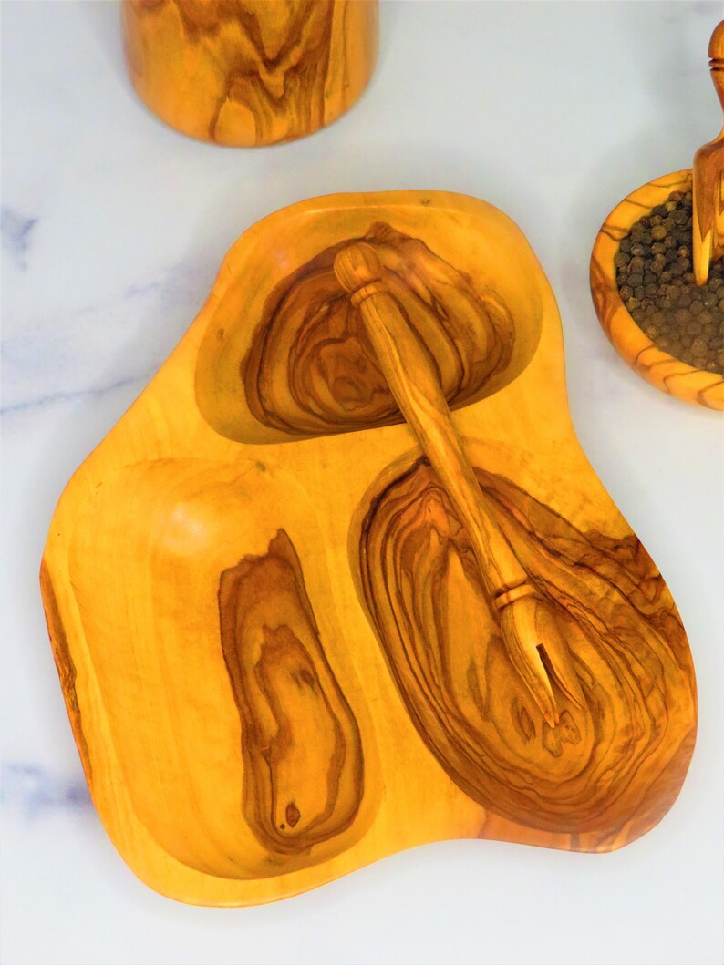 May include: A wooden serving dish with three compartments, one with a small wooden spoon. The dish is made of olive wood and has a natural, rustic finish.