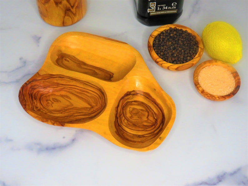 May include: A wooden serving tray with three separate bowls. The tray is made of olive wood and has a natural wood grain pattern. The bowls are perfect for serving snacks, dips, or condiments.