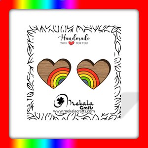 May include: A pair of wooden heart-shaped earrings with a rainbow design. The earrings are handmade and feature a brown wood grain with a rainbow of colors in the center of each heart. The text "Handmade with love for you" is visible in the image.