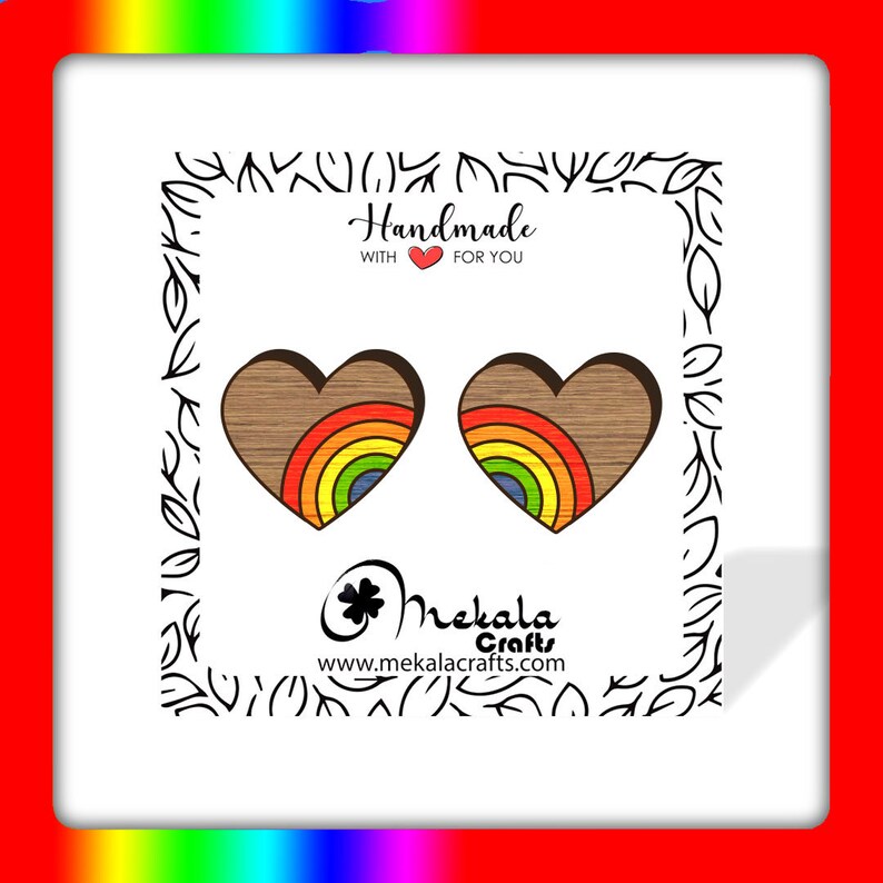 May include: A pair of wooden heart-shaped earrings with a rainbow design. The earrings are handmade and feature a brown wood grain with a rainbow of colors in the center of each heart. The text "Handmade with love for you" is visible in the image.
