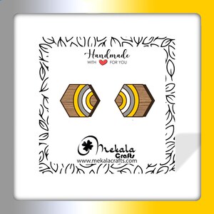 May include: A pair of hexagonal wooden earrings with yellow, white, and brown stripes. The earrings are handmade and feature a wood grain pattern. The text "Handmade with &hearts; for you" is visible in the image.