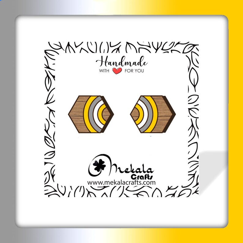 May include: A pair of hexagonal wooden earrings with yellow, white, and brown stripes. The earrings are handmade and feature a wood grain pattern. The text "Handmade with &hearts; for you" is visible in the image.