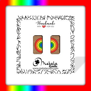 May include: A pair of rainbow wooden earrings with a brown background. The earrings are handmade and feature a rainbow design with red, orange, yellow, green, blue, indigo, and violet colors. The text "Handmade with &hearts; for you" is visible in the image.