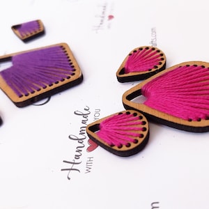 May include: A set of four wooden earrings with thread woven into the design. Two earrings are pink and two are purple.