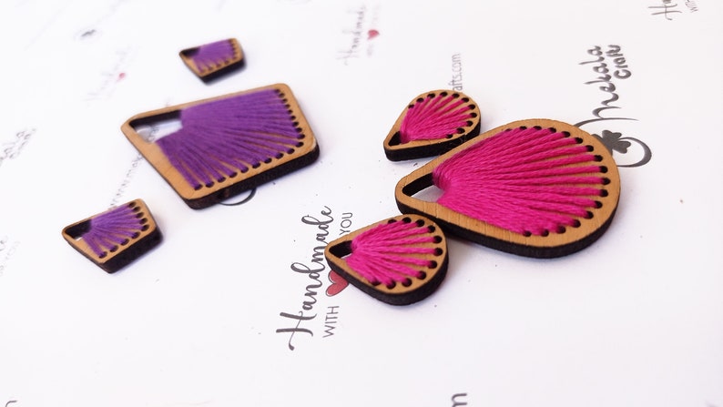 May include: A set of four wooden earrings with thread woven into the design. Two earrings are pink and two are purple.