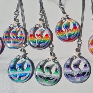 May include: A collection of seven round pendant necklaces with silver chains. Each pendant features a colorful, abstract design within a clear resin. The designs include rainbow, blue, green, and purple color schemes. Each necklace has a small star charm.