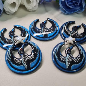 May include: Five blue and black loon pendants with a white star accent. Each pendant features a loon design with white dot detailing and red eyes. The pendants are circular with a glossy finish, perfect for jewelry making.