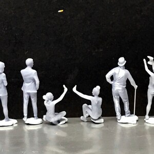 May include: A set of nine gray figurines of people in various poses. The figurines are standing on a gray surface.