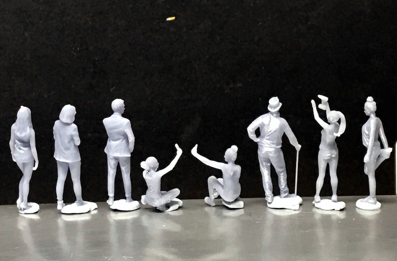 May include: A set of nine gray figurines of people in various poses. The figurines are standing on a gray surface.