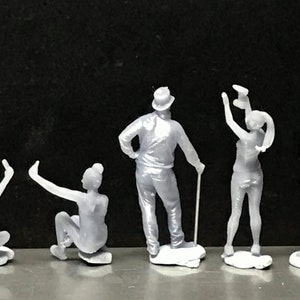 May include: Five gray 3D printed figurines of people in various poses. The figures are standing on small white bases.