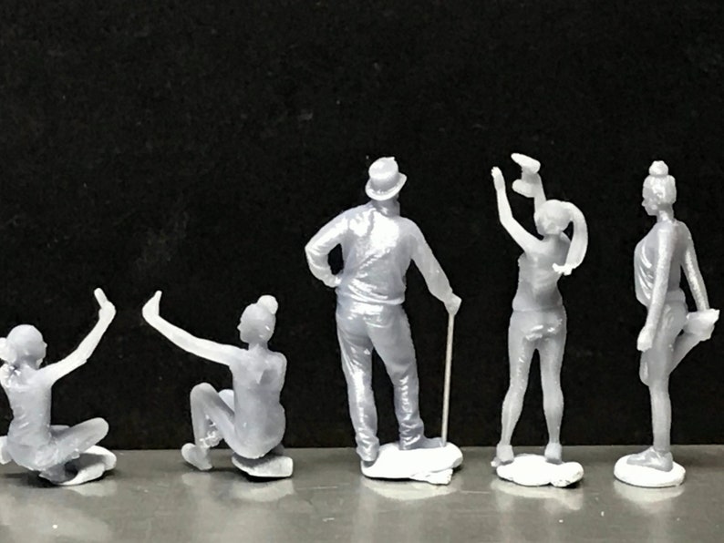 May include: Five gray 3D printed figurines of people in various poses. The figures are standing on small white bases.