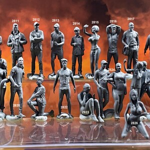 May include: A collection of 17 small, gray, 3D printed figurines of people in various poses. The figurines are arranged in two rows on a clear surface.