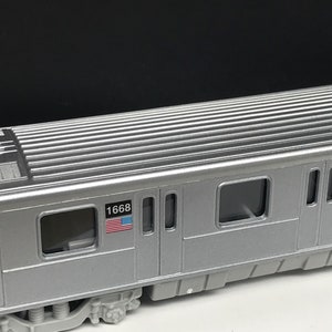 K&ouml;nnte beinhalten: Ein silberner Modellzugwagen mit der Nummer "1668" und einer amerikanischen Flagge, die auf der Seite aufgedruckt ist. Der Wagen hat mehrere Fenster und ein geripptes Dach.