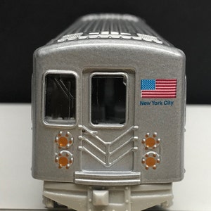 K&ouml;nnte beinhalten: Ein silbernes Spielzeugmodell eines New Yorker U-Bahn-Wagens mit einer amerikanischen Flagge und dem Schriftzug "New York City" an der Seite.