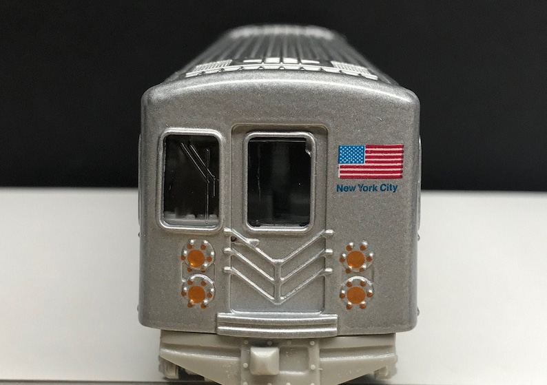 K&ouml;nnte beinhalten: Ein silbernes Spielzeugmodell eines New Yorker U-Bahn-Wagens mit einer amerikanischen Flagge und dem Schriftzug "New York City" an der Seite.
