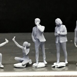 May include: Five gray 3D printed figurines of people in various poses. The figurines are standing on small bases.