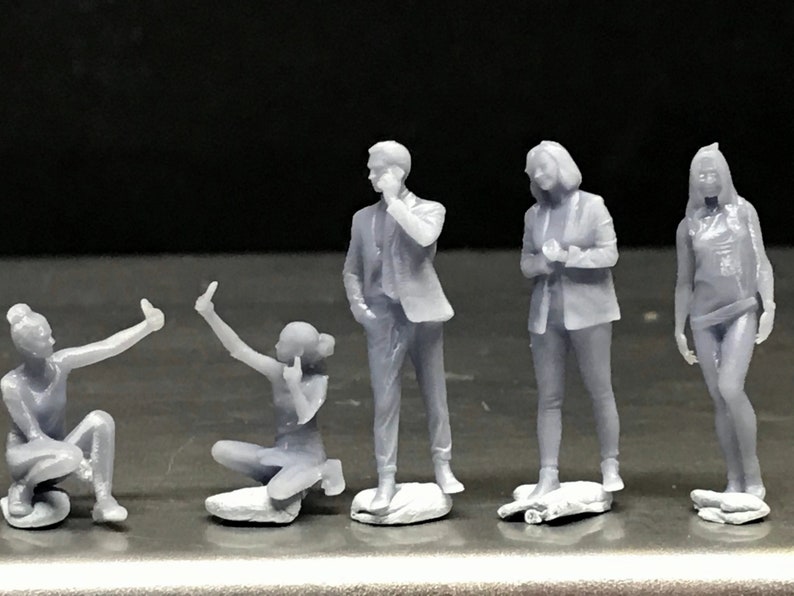 May include: Five gray 3D printed figurines of people in various poses. The figurines are standing on small bases.