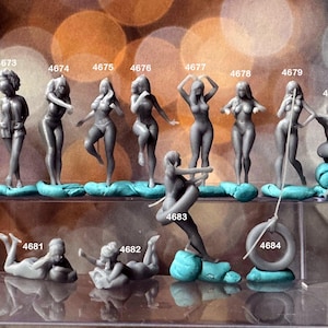 May include: A collection of 12 gray resin figurines of women in various poses. The figurines are arranged on a shelf with a blue background. The figurines are numbered 4672 through 4684.