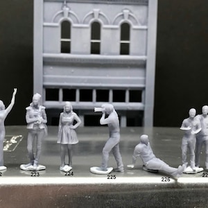 May include: Seven 3D printed figurines of people in various poses, including a person raising their arms, a person holding a camera, and a couple standing together. The figurines are gray and are numbered 222 through 227.