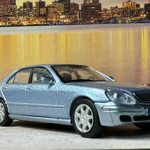 May include: A silver-grey model car of a Mercedes-Benz S-Class sedan with a black interior. The car has a license plate that reads "S1SV 705".