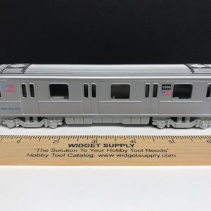 K&ouml;nnte beinhalten: Ein silbernes Spielzeugmodell eines New Yorker U-Bahn-Wagens mit der Nummer 1668 an der Seite. Der Wagen hat eine blau-wei&szlig;e amerikanische Flagge an der Seite und die Worte "New York City" sind an der Seite aufgedruckt.