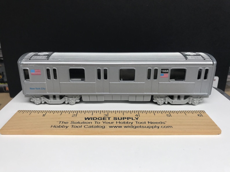 K&ouml;nnte beinhalten: Ein silbernes Spielzeugmodell eines New Yorker U-Bahn-Wagens mit der Nummer 1668 an der Seite. Der Wagen hat eine blau-wei&szlig;e amerikanische Flagge an der Seite und die Worte "New York City" sind an der Seite aufgedruckt.