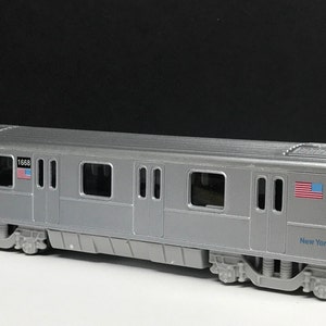 K&ouml;nnte beinhalten: Ein silbernes Spielzeugmodell eines New Yorker U-Bahn-Wagens mit der Nummer "1668" und einer amerikanischen Flagge an der Seite. Der Wagen tr&auml;gt auch den Schriftzug "New York City" an der Seite.