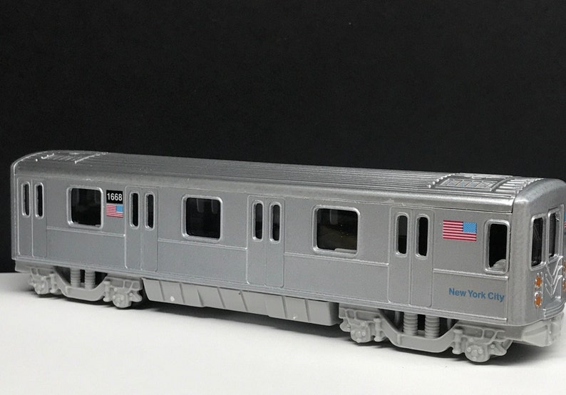 K&ouml;nnte beinhalten: Ein silbernes Spielzeugmodell eines New Yorker U-Bahn-Wagens mit der Nummer "1668" und einer amerikanischen Flagge an der Seite. Der Wagen tr&auml;gt auch den Schriftzug "New York City" an der Seite.