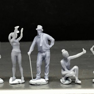 May include: Five gray 3D printed figurines of people in various poses. The figurines are standing on small gray bases.