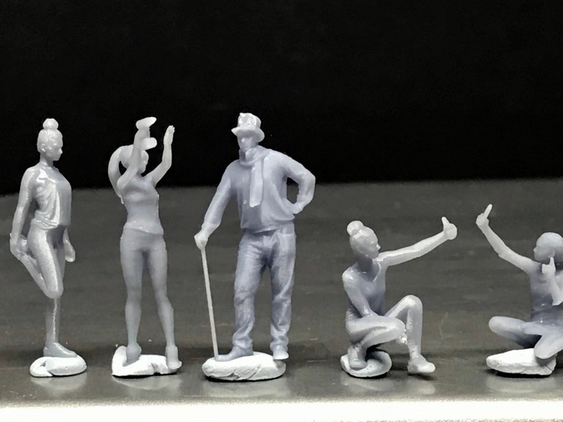 May include: Five gray 3D printed figurines of people in various poses. The figurines are standing on small gray bases.