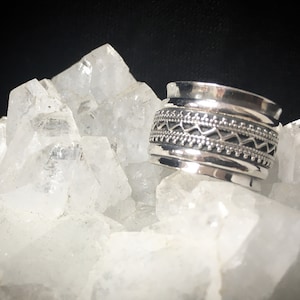 Può includere: Un anello d'argento con un design geometrico. L'anello è composto da più bande con dettagli intricati.