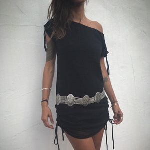 May include: Black off-the-shoulder dress with drawstring details and a silver-toned belt. The dress has short sleeves with tie accents. The belt features ornate oval medallions. The dress is a casual, stylish garment.