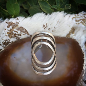 Puede incluir: Un anillo de plata con un diseño geométrico. El anillo está hecho de varios círculos concéntricos.