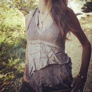 Può includere: Una donna indossa un top halter marrone lavorato a uncinetto con una collana e orecchini d'argento. È in piedi in una zona boscosa.