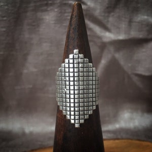 May include: A silver ring with a geometric design. The ring is on a wooden display stand.