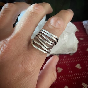 Könnte beinhalten: Ein silberner Ring mit einem wellenförmigen, organischen Design. Der Ring besteht aus mehreren Silberbändern, die verdreht und miteinander verflochten sind.