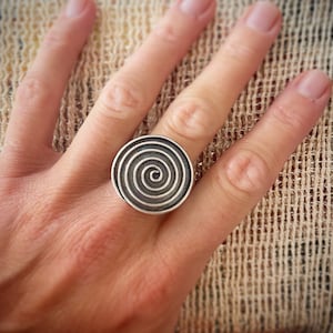 Può includere: Un anello d'argento con un design circolare che presenta un motivo a spirale.