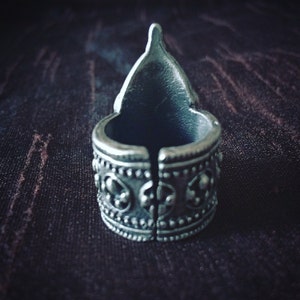 May include: A silver ring with a pointed top and intricate designs around the band.