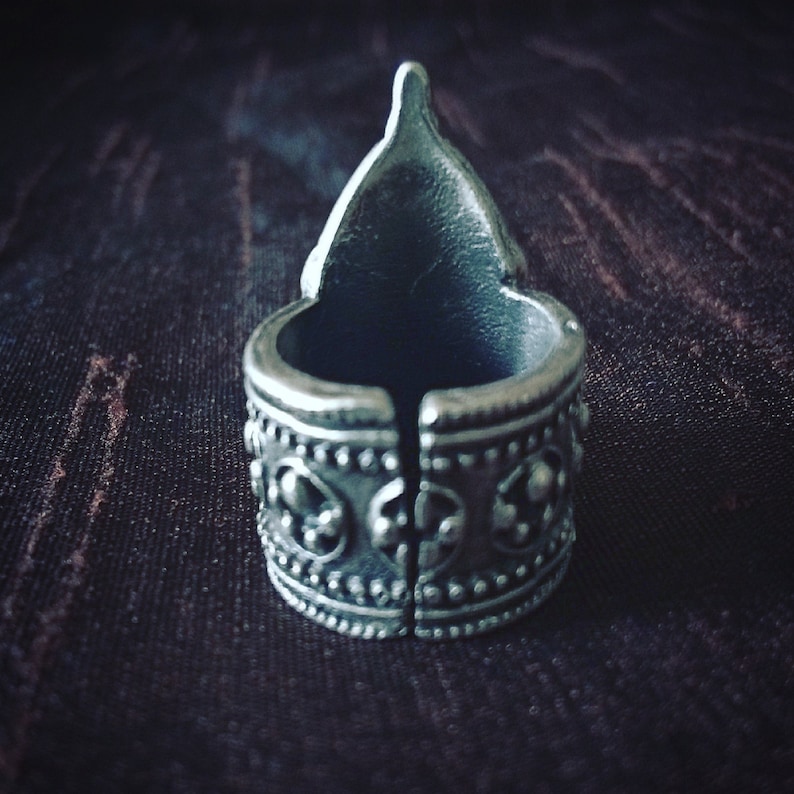 May include: A silver ring with a pointed top and intricate designs around the band.