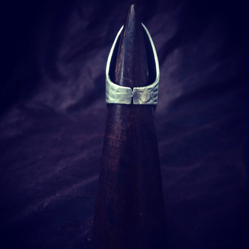 May include: A silver ring with a textured surface, displayed on a wooden ring holder.