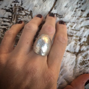 Peut inclure: Une bague en argent martelé de forme ovale arrondie. La bague est portée au doigt.