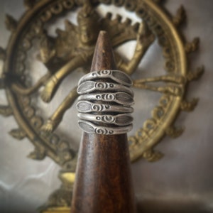 Può includere: Un anello d'argento con un design decorativo di motivi a spirale e foglie. L'anello è esposto su un supporto in legno.