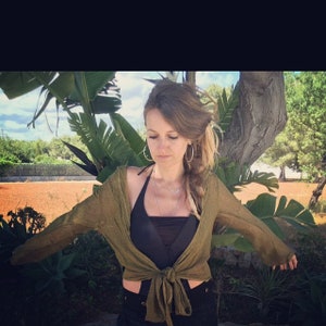 May include: A woman wearing a green cardigan tied at the waist over a black halter top. She has long brown hair with a braid and is wearing hoop earrings.