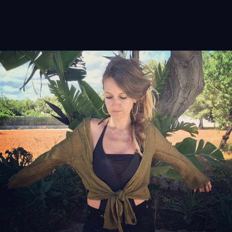 May include: A woman wearing a green cardigan tied at the waist over a black halter top. She has long brown hair with a braid and is wearing hoop earrings.
