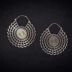 May include: A pair of silver hoop earrings with a delicate, intricate design. The earrings are circular and feature a mandala-like pattern with a central circle.