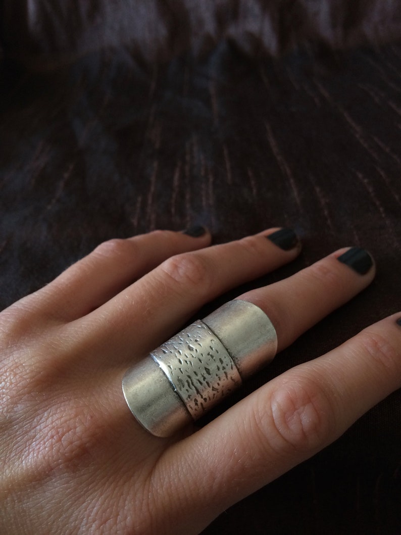 May include: A silver ring with a textured band and two smooth bands. The ring is worn on a finger. The ring has a modern, minimalist design.