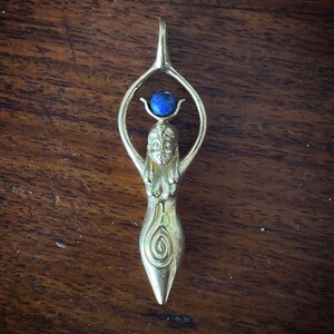 K&ouml;nnte beinhalten: Ein goldener Anh&auml;nger mit einer stilisierten Frauenfigur und einem blauen Edelstein oben. Der Anh&auml;nger hat ein Spiralmuster am unteren Teil.