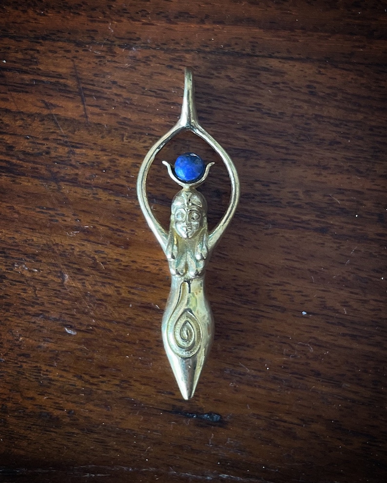 K&ouml;nnte beinhalten: Ein goldener Anh&auml;nger mit einer stilisierten Frauenfigur und einem blauen Edelstein oben. Der Anh&auml;nger hat ein Spiralmuster am unteren Teil.